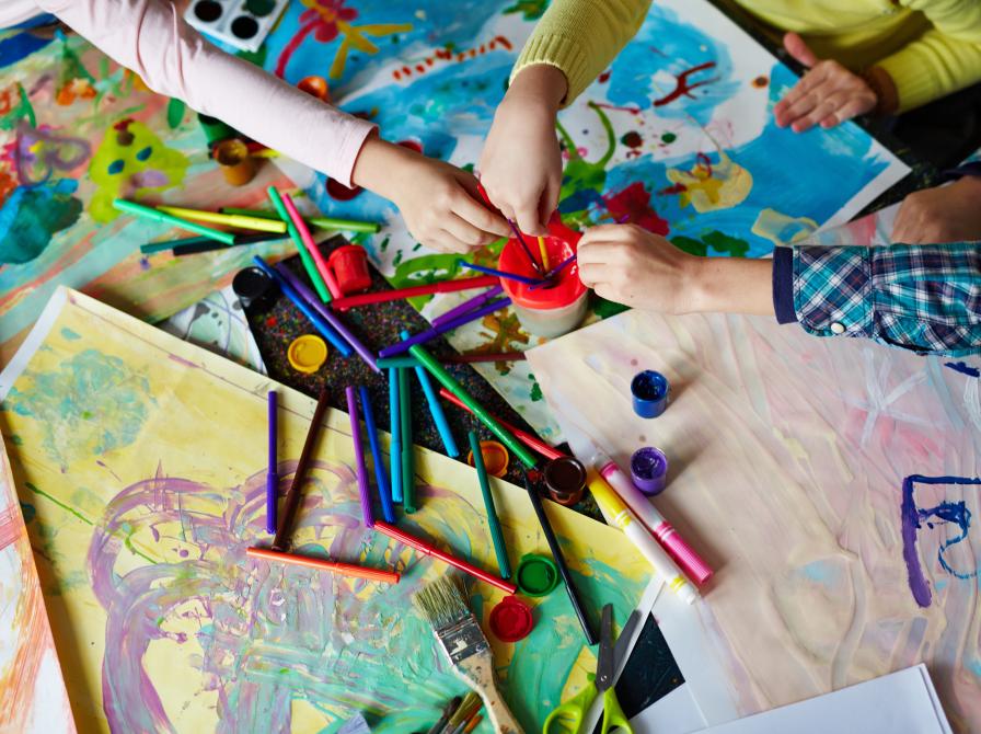 Børnehænder der rækker ind over papir, maling og pensler